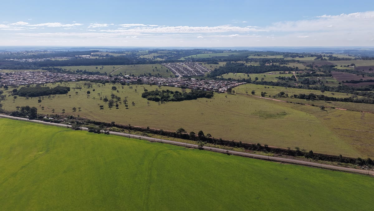 Vista aérea de um terreno amplo com o bairro e a área rural do entorno ao fundo